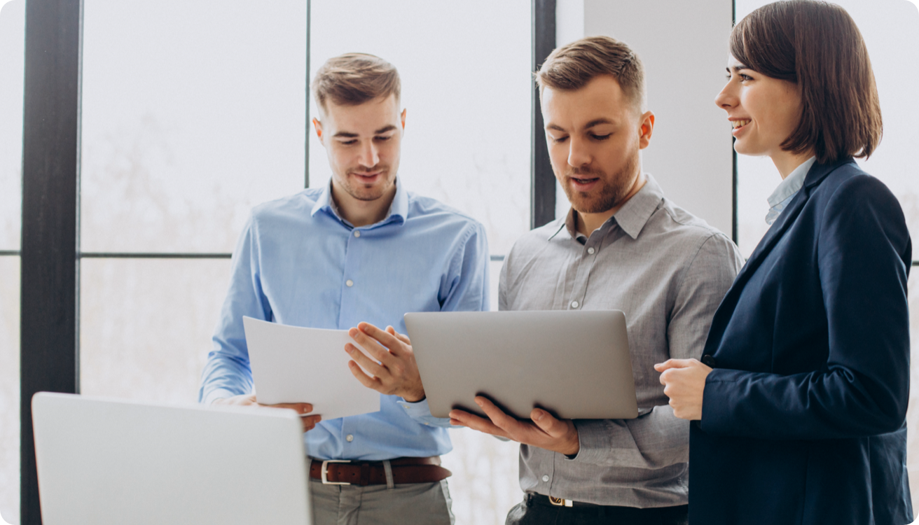 Three people discuss a document while holding a laptop computer