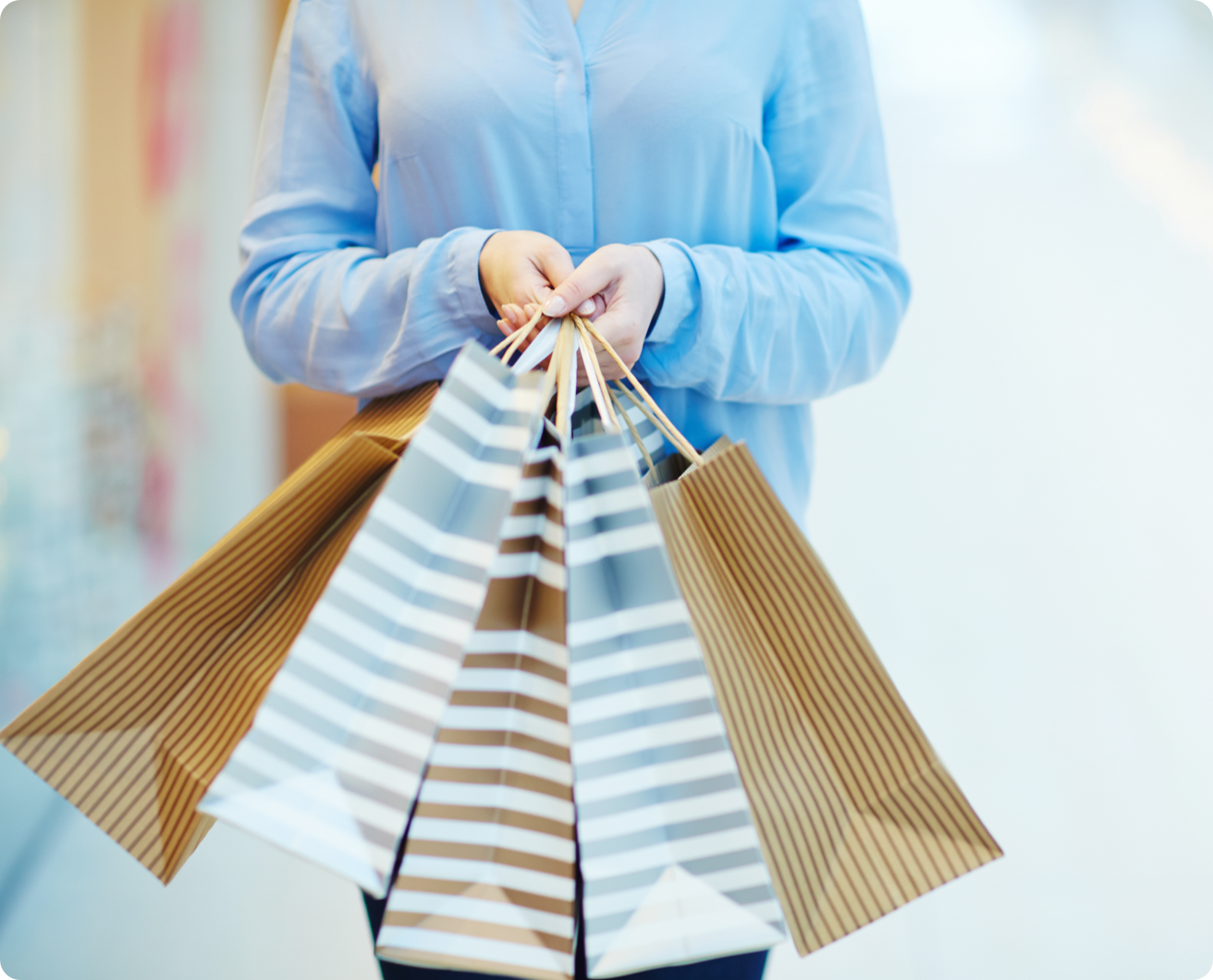 Person wearing a blue button down shirt, holding four striped shopping bags.
