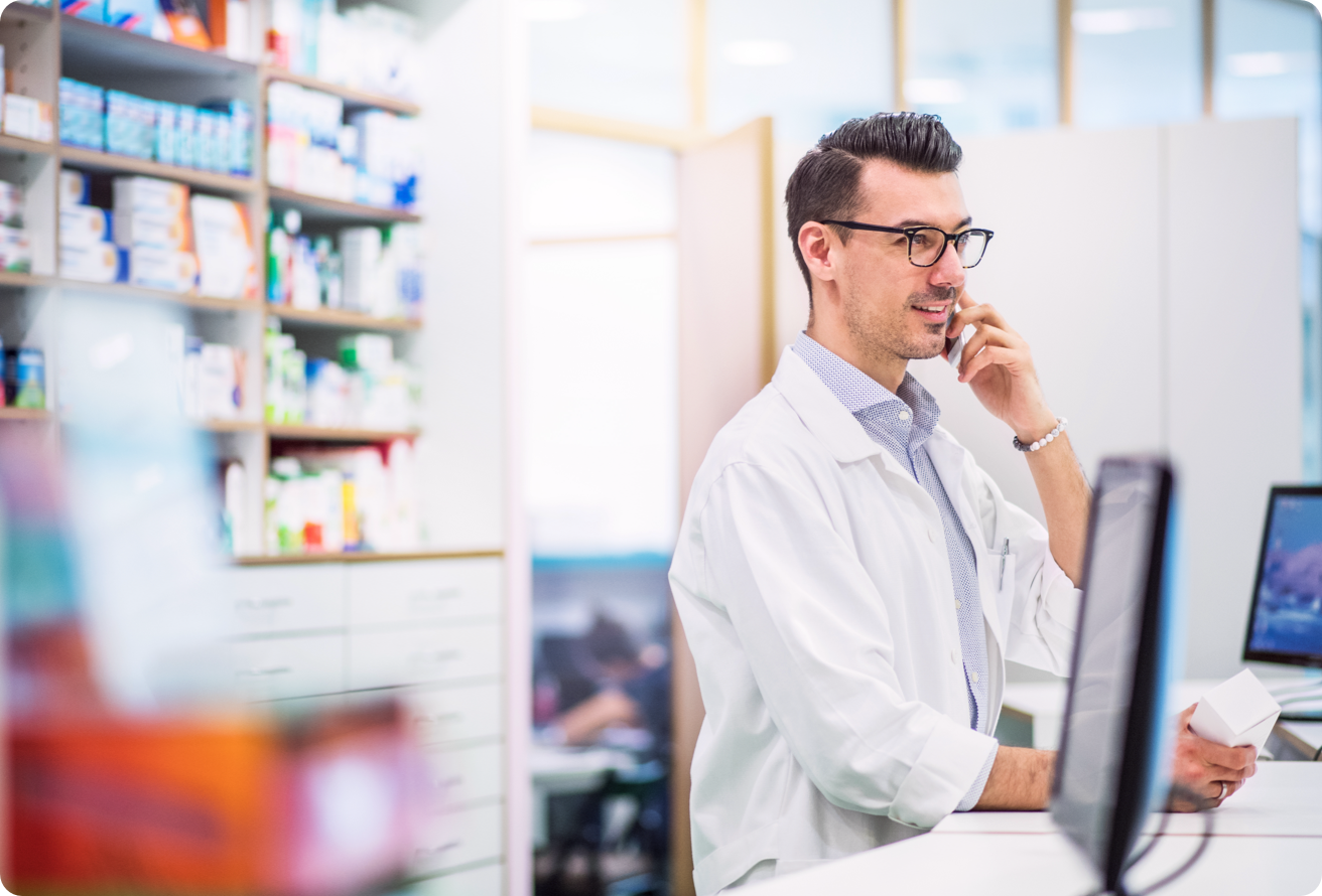 A pharmacist behind a counter, talking on the phone. 