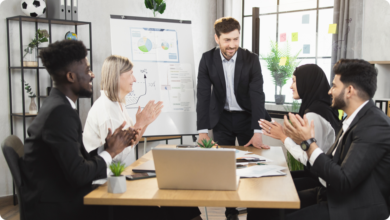 A diverse group of people clap for a presentation around a conference table