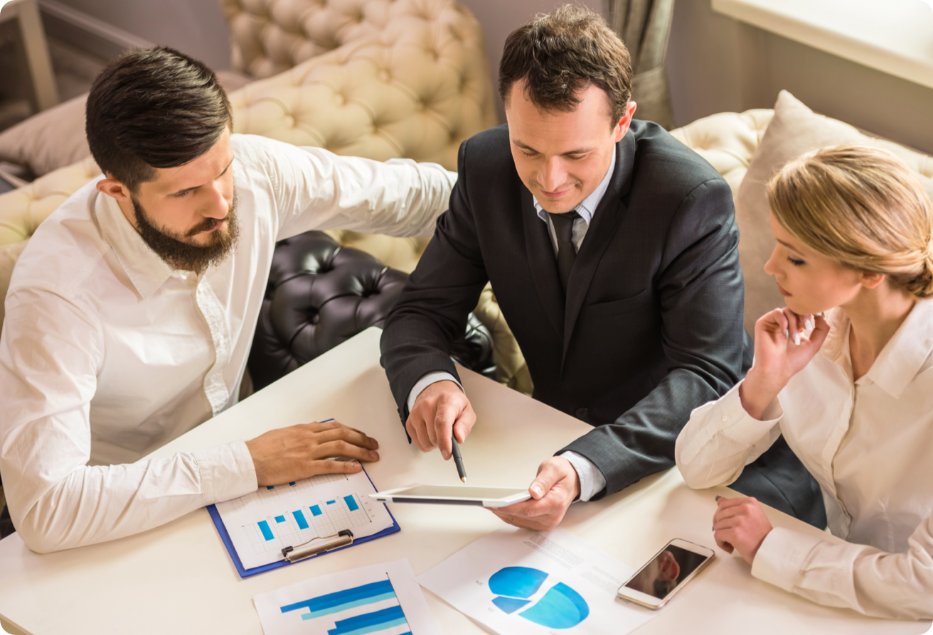 Three people conducting a meeting, seated at a table, looking at graphs and charts.